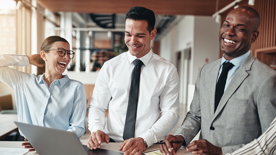 Three people smiling and one person holding a laptop.